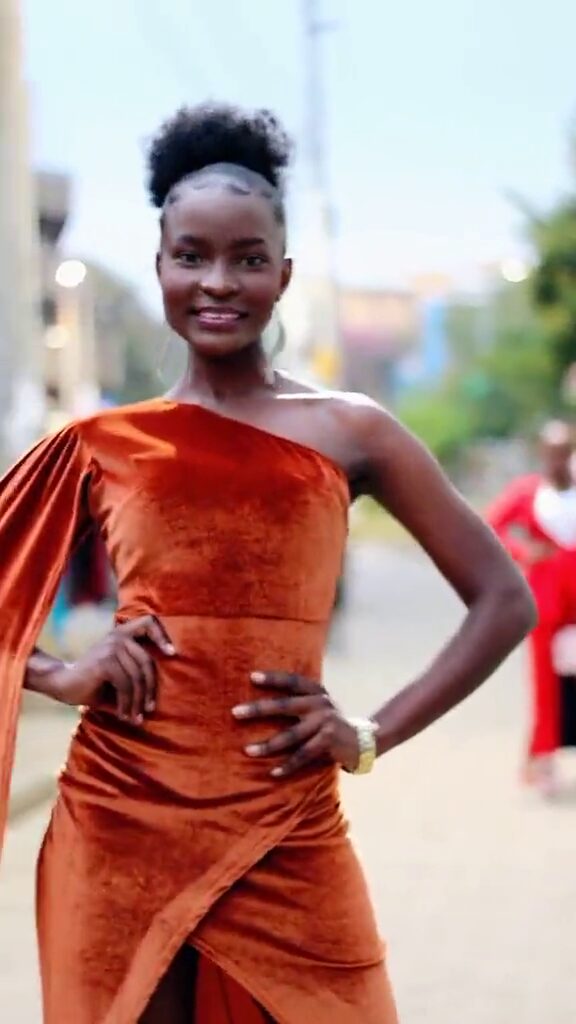 Leah Akoth Ochieng on a street in Kisumu, in a rust-coloured one-shoulder velvet gown, shooting with DALA Commercial Models.